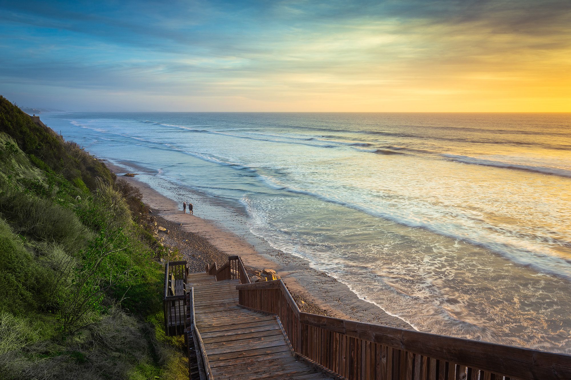 Wooden staircase descending a bluff to a Southern California beach at sunset